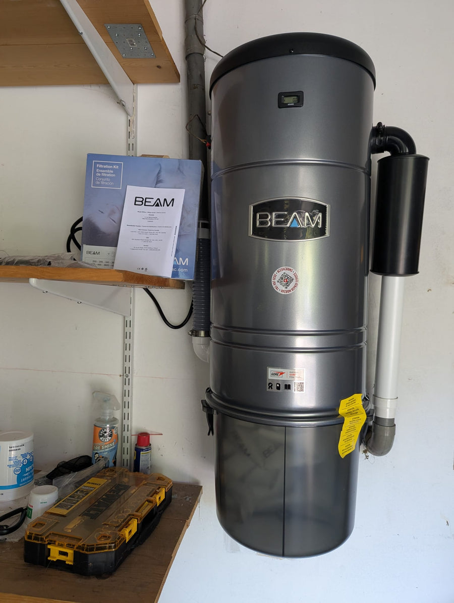 BEAM central vacuum power unit with connected piping and Ace Vacuums service label at a customer home
