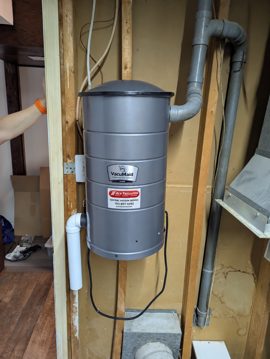 VacuMaid central vacuum power unit mounted on wooden studs with connected piping and an AceVacuums service sticker at AceVacuums