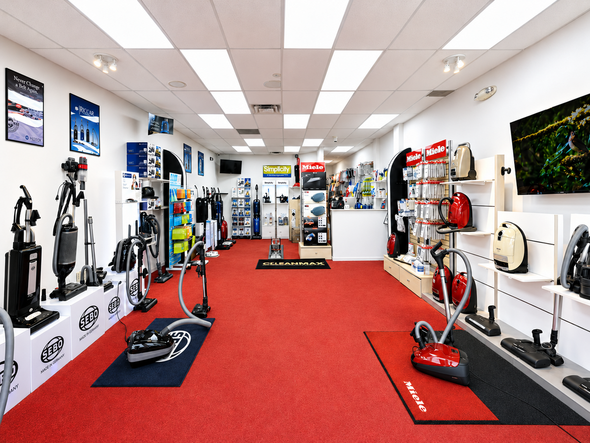 SEBO upright and Miele canister vacuums with accessories displayed along a red-carpet aisle at Ace Vacuums